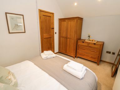 A bedroom with a bed, wooden door, wooden wardrobe, wooden dresser with flowers in a vase and folded towels at Swallows Nest Whitby