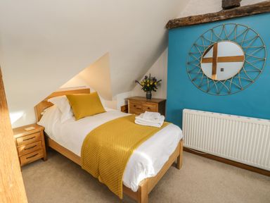 A bedroom with a single bed yellow bedding wooden furniture a blue wall with a round mirror and a radiator at Swallows Nest in Whitby