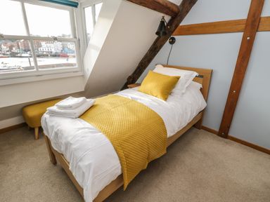 A bedroom with a single bed with yellow bedding and pillows near a window overlooking a waterfront at Swallows Nest in Whitby