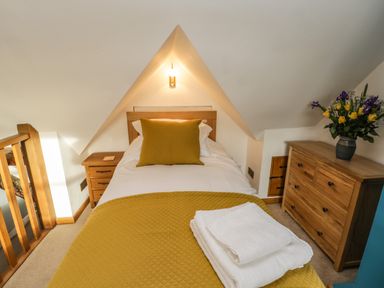 A bedroom with a single bed yellow pillow and blanket wooden bedside table wooden chest of drawers with flowers at Swallows Nest in Whitby