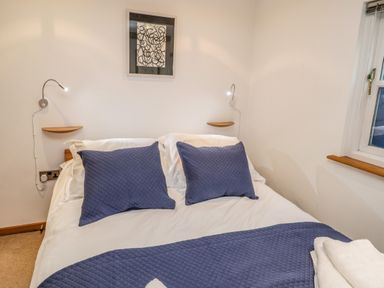A bedroom with a bed with blue pillows and a bedspread a window and wall lamps at Swallows Nest in Whitby