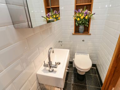 A small bathroom with a white sink and toilet and a wooden shelf with a vase of flowers at Swallows Nest in Whitby
