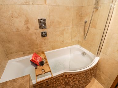 A bathroom with a bathtub filled with bubbles and a wooden tray holding a book and a glass of wine at Swallows Nest in Whitby