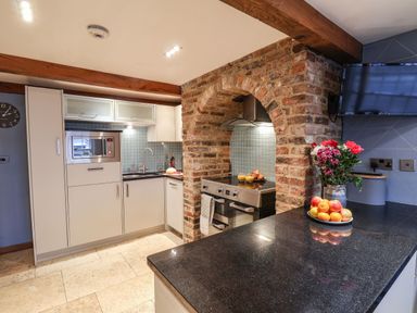 A kitchen with a brick oven arch, stainless steel stove, beige cabinets, a black countertop with flowers and fruit at Swallows Nest in Whitby