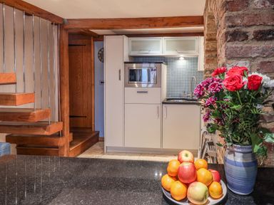 A kitchen area with microwave oven and sink beside a wooden staircase with flowers and fruit on a countertop at Swallows Nest in Whitby