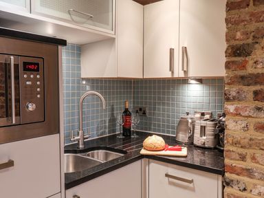 A kitchen corner with a sink wine bottle two glasses bread and vegetables on a cutting board kettle toaster and coffee machine at Swallows Nest in Whitby