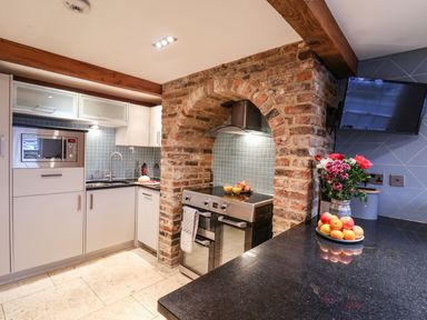 A kitchen with white cabinets a microwave oven a brick arch with a stove countertop with fruit and flowers at Swallows Nest in Whitby