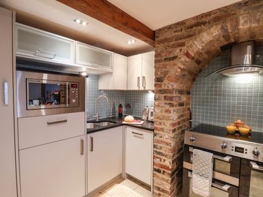 A kitchen with white cabinets a microwave a sink a brick arch and a stove with food on it at Swallows Nest in Whitby