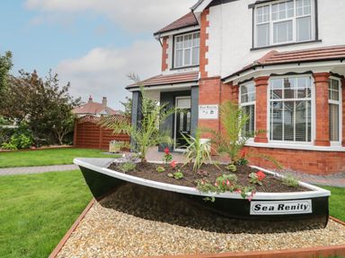 A boat-shaped garden planter with plants and flowers in front of a brick and white two-story house at 23 Carmen Sylva Road in Llandudno