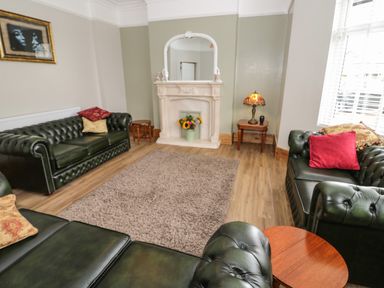 A living room with green leather sofas a fireplace flower vase and a window at 23 Carmen Sylva Road in Llandudno