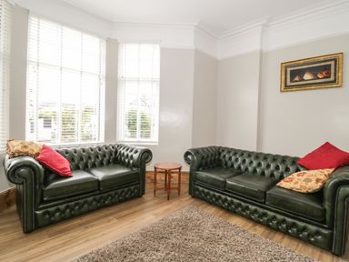 A living room with two green leather sofas with cushions and a small wooden table between them at 23 Carmen Sylva Road in Llandudno