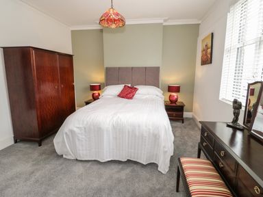A bedroom with a bed a wardrobe bedside tables lamps a dresser with a mirror and a striped bench at 23 Carmen Sylva Road in Llandudno