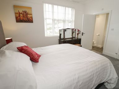 A bedroom with a bed a dresser with a mirror and an open door showing a bathroom at 23 Carmen Sylva Road in Llandudno