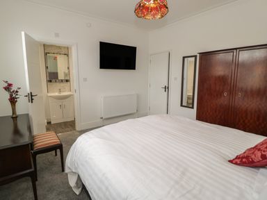 A bedroom with a bed a wooden wardrobe a wall-mounted television and a desk with a chair at 23 Carmen Sylva Road in Llandudno
