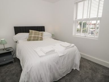 A bedroom with a bed white linens and towels on top a checkered pillow bedside tables with lamps and a window with blinds at 23 Carmen Sylva Road in Llandudno