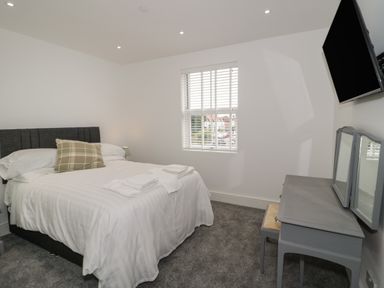 A bedroom with a bed a green plaid pillow a gray vanity table with mirror and a wall-mounted TV at 23 Carmen Sylva Road in Llandudno