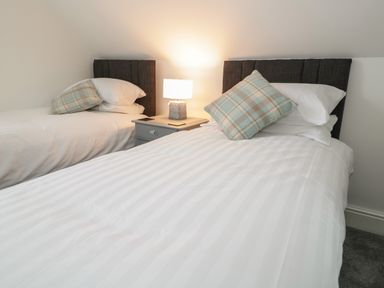 A bedroom with two single beds a bedside table with a lamp and pillows at 23 Carmen Sylva Road in Llandudno