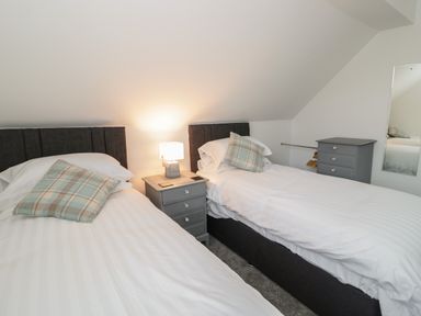 A bedroom with two single beds a nightstand with a lamp between the beds and a dresser with a mirror at 23 Carmen Sylva Road in Llandudno