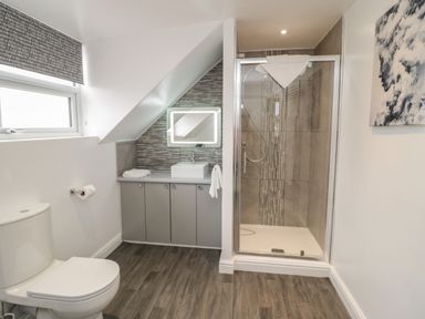 A bathroom with a toilet sink vanity under a sloped ceiling and a glass shower enclosure at 23 Carmen Sylva Road in Llandudno
