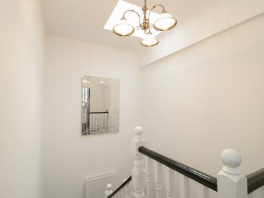 A staircase with white balusters and a black handrail a wall mirror and a ceiling light at 23 Carmen Sylva Road in Llandudno