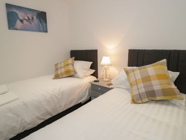 A bedroom with two single beds a nightstand with a lamp and a wall painting at 23 Carmen Sylva Road in Llandudno