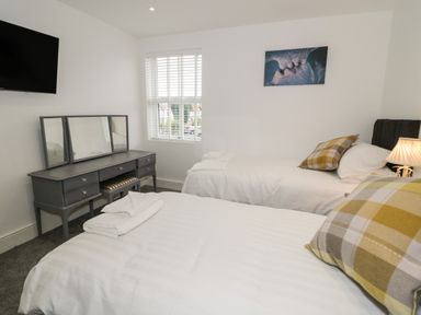 A bedroom with two single beds a dressing table a window and a wall mounted television at 23 Carmen Sylva Road in Llandudno