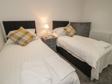 A bedroom with two single beds a nightstand with a lamp between beds and a gray chest of drawers at 23 Carmen Sylva Road in Llandudno