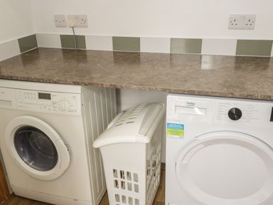 A laundry room with a washing machine dryer and laundry basket at 23 Carmen Sylva Road in Llandudno