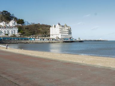 A beach with a promenade and a large white hotel on a hill near a sea pier at 23 Carmen Sylva Road in Llandudno