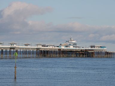 A wooden pier extending over the sea with a large building on it under a cloudy sky at 23 Carmen Sylva Road in Llandudno