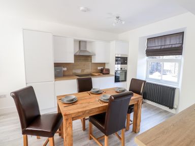 A kitchen with a wooden dining table set with four place settings and four brown chairs at 8 Waterhead Terrace Ambleside