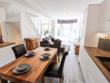 A kitchen and dining area with wooden table and chairs next to a living room with a sofa and large windows at 8 Waterhead Terrace Ambleside