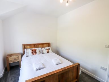 A bedroom with a wooden bed and bedside table with white walls at 8 Waterhead Terrace in Ambleside