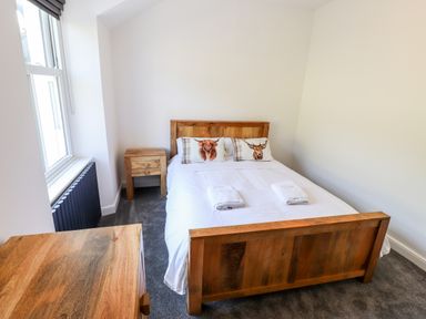 A bedroom with a wooden bed, bedside table, and dresser at 8 Waterhead Terrace in Ambleside
