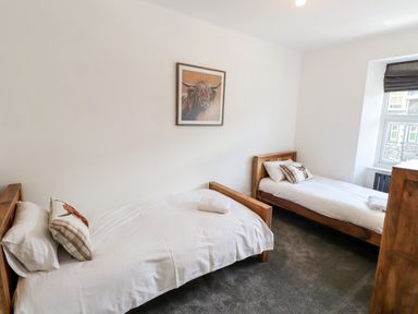 A bedroom with two single wooden beds white bedding a framed animal picture on the wall and a window with blinds at 8 Waterhead Terrace Ambleside