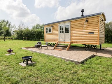 A wooden shepherds hut with steps and outdoor chairs on a gravel area with grass and a fire pit at Waylands in Uffington