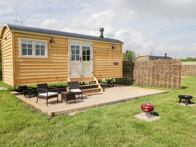 A wooden cabin on wheels with outdoor chairs and table on a gravel patio and grills on grass at Waylands in Uffington