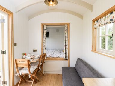 A small dining area with wooden chairs and a table next to a bed area and a gray sofa in a compact room at Waylands in Uffington