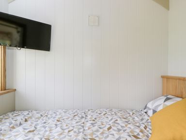 A bedroom with a bed featuring geometric patterned bedding a yellow pillow a mounted television and white paneled walls at Waylands in Uffington