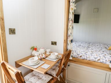 A small dining table set with dishes and two wooden chairs next to a bed with patterned bedding at Waylands in Uffington