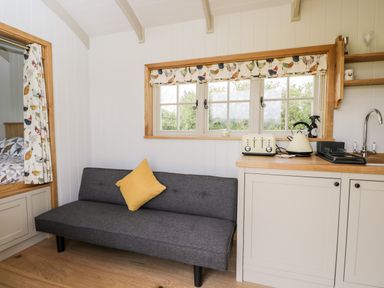 A small living area with a gray sofa and yellow pillow near a kitchenette with toaster kettle and sink at Waylands in Uffington