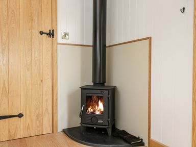 A wood burning stove with fire inside next to a wooden door in a corner of a room at Waylands in Uffington