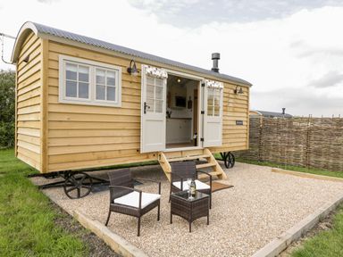 A small wooden cabin on wheels with open double doors and outdoor chairs with a table at Waylands in Uffington