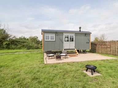A small grey corrugated metal cabin with double doors and windows on a gravel patio with two chairs and a table on grass at Ridgeway in Uffington