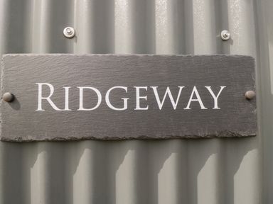 A slate sign with the word Ridgeway mounted on a corrugated metal wall at Ridgeway in Uffington