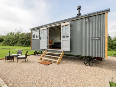 An outdoor seating area with two chairs and a small table next to a grey corrugated metal shepherds hut with open double doors at Ridgeway in Uffington