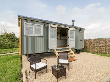 A small grey corrugated metal cabin with open French doors and two chairs with a table outside at Ridgeway in Uffington