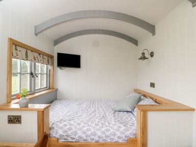 A bedroom with a bed under arched ceiling with wooden frame window and mounted television at Ridgeway in Uffington