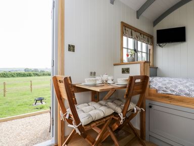 A small dining area with wooden chairs and table set for tea next to a window and open door showing outdoor greenery at Ridgeway in Uffington