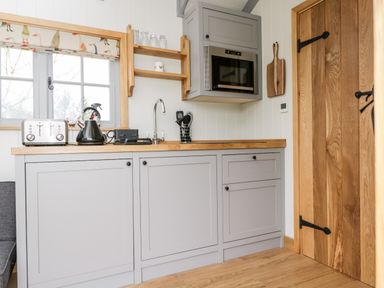 A kitchen with grey cabinets wooden countertop a microwave toaster kettle utensils and a wooden door at Ridgeway in Uffington